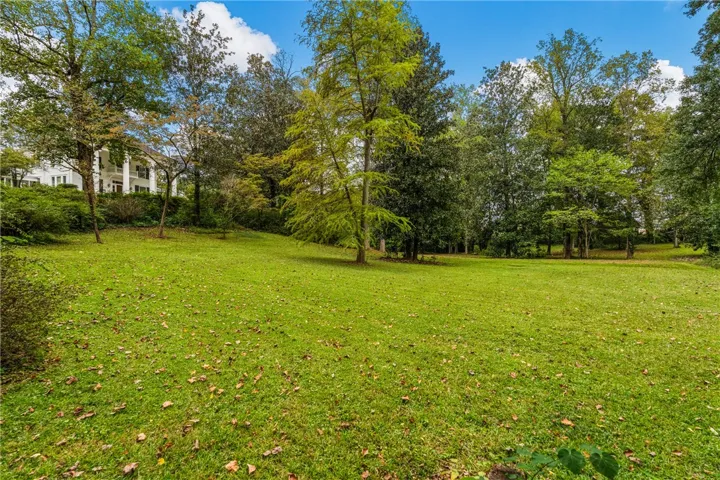 Mature trees frame a sprawling, lush green lawn situated on a gently sloping hillside.