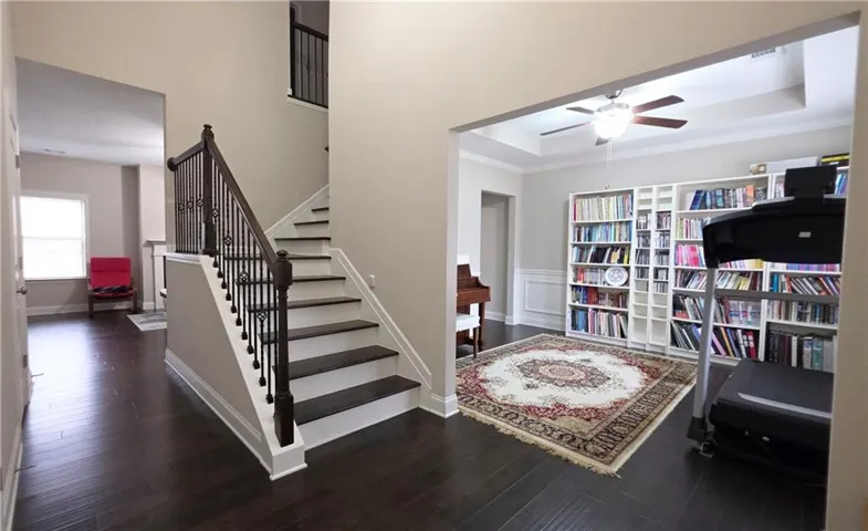 Rich hardwood floors and a modern staircase frame a versatile adjacent living space.