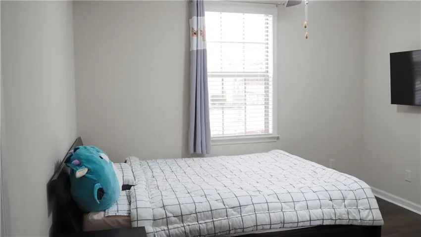 A quiet bedroom features neutral walls and dark wood-toned flooring.