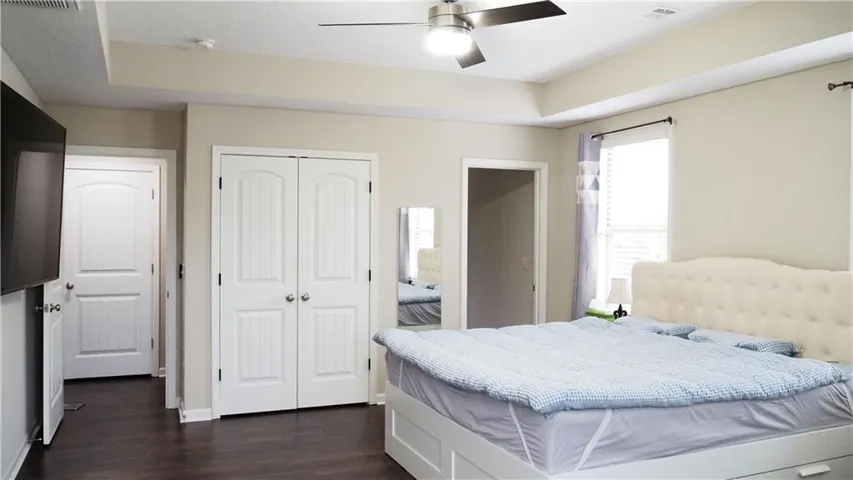 A spacious bedroom features elegant tray ceilings and dark wood flooring.