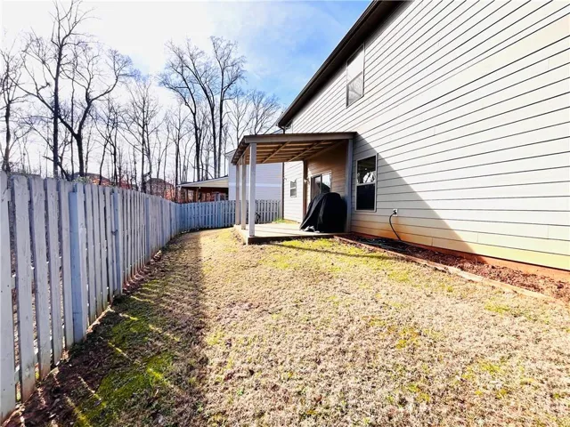 A wooden privacy fence borders the grassy yard alongside a covered patio.