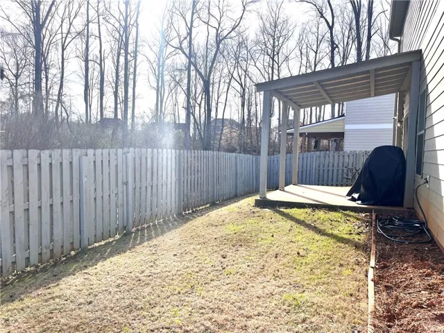 A wooden privacy fence surrounds the grassy backyard, featuring a covered patio area.