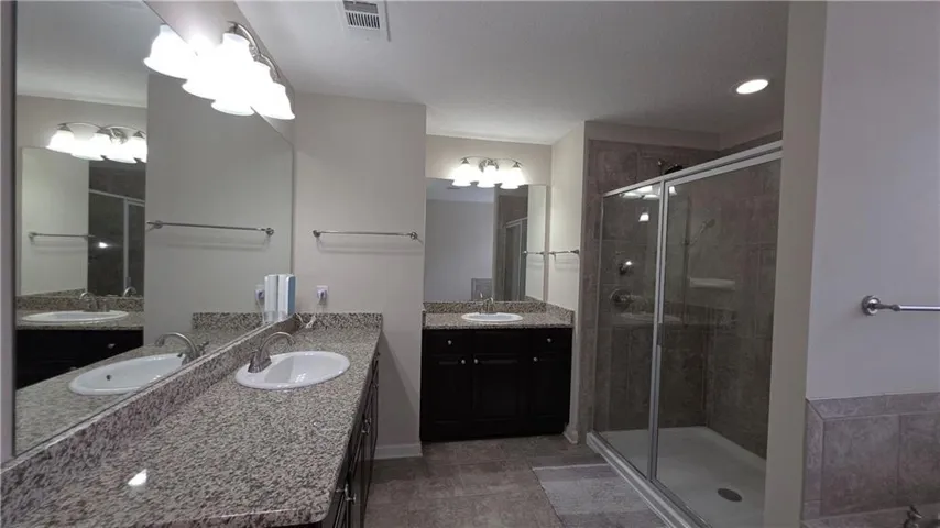 Double vanities with stone counters flank a glass-enclosed shower with tiled walls.
