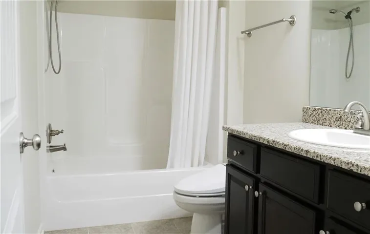 A classic tub and shower combination sits adjacent to a dark vanity with stone countertops.