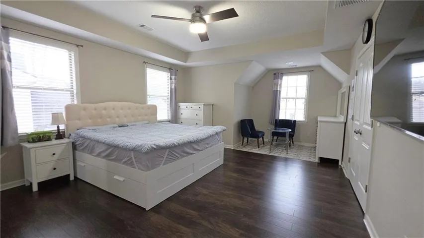 Rich wood floors anchor this expansive bedroom retreat beneath a tray ceiling.