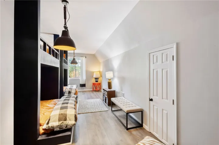 A spacious bedroom features sloped ceilings, durable plank flooring, and classic white woodwork.