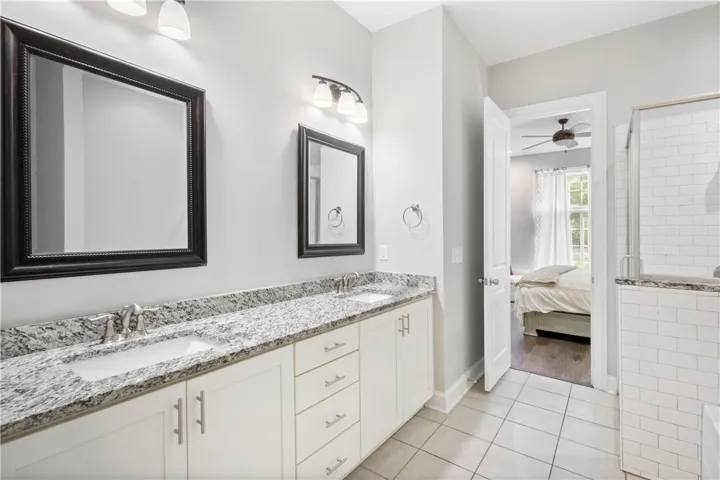 Clean lines and stone counters define this well-appointed space with dual vanities and tile flooring.