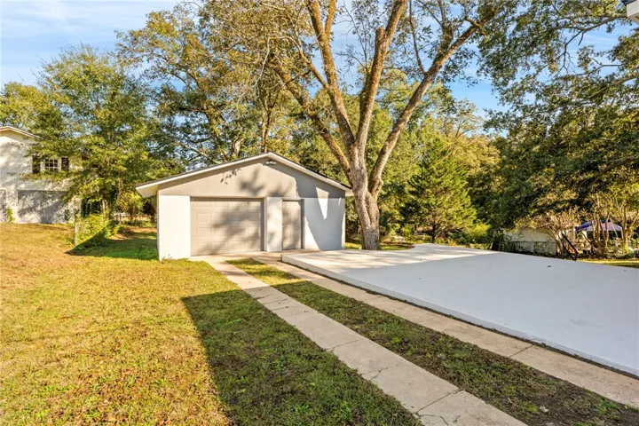 A detached garage sits alongside a spacious concrete parking pad under mature shade trees.