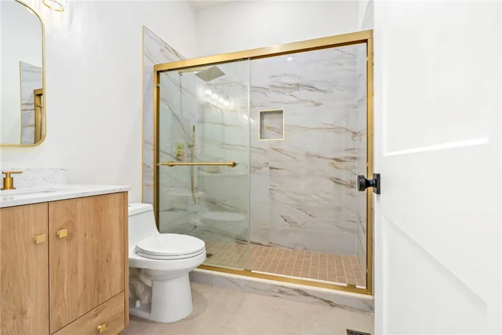 A modern bathroom highlights a walk-in shower framed in gold alongside marble-patterned tile walls.