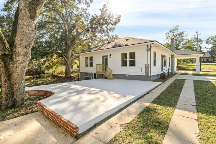 Mature trees frame a concrete patio area and parking pad behind this classic siding home.