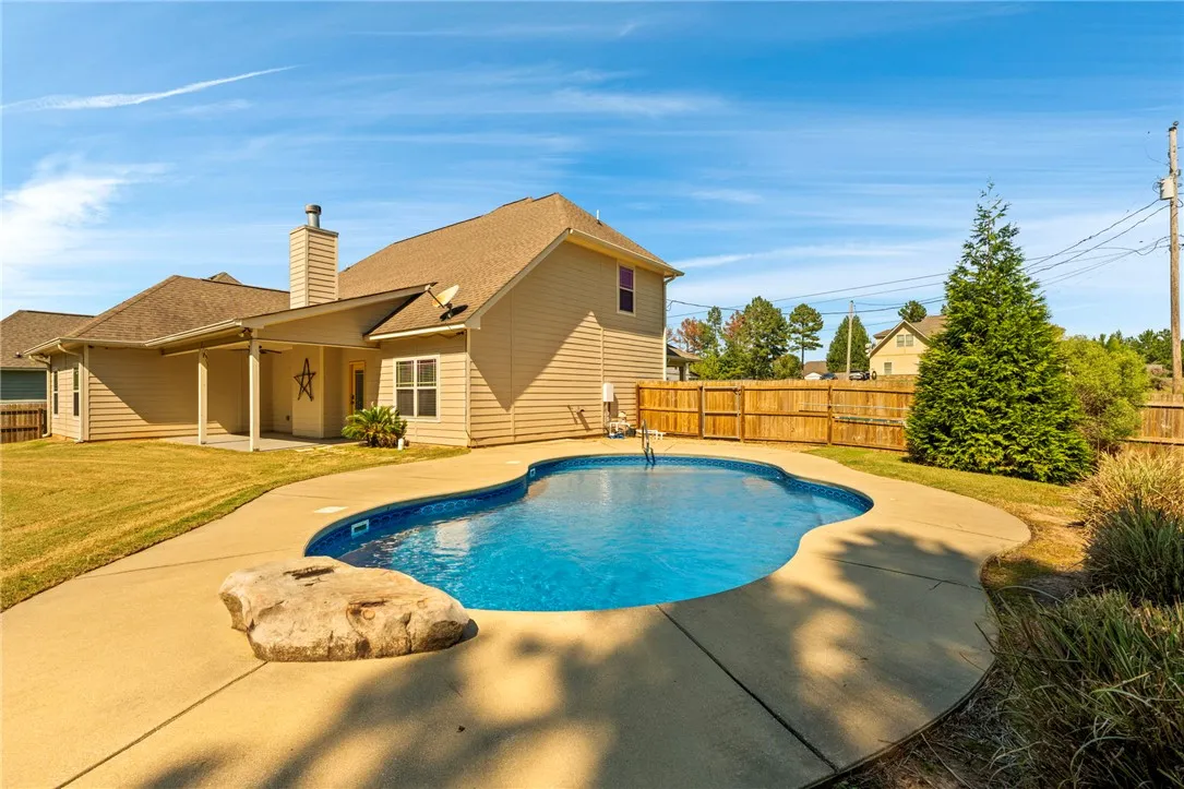 A spacious backyard patio surrounds a sparkling swimming pool under clear blue skies.