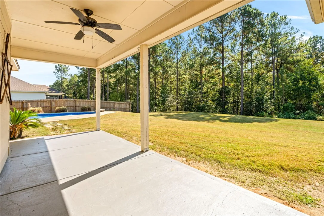 An inviting covered concrete patio overlooks a grassy backyard framed by mature trees.
