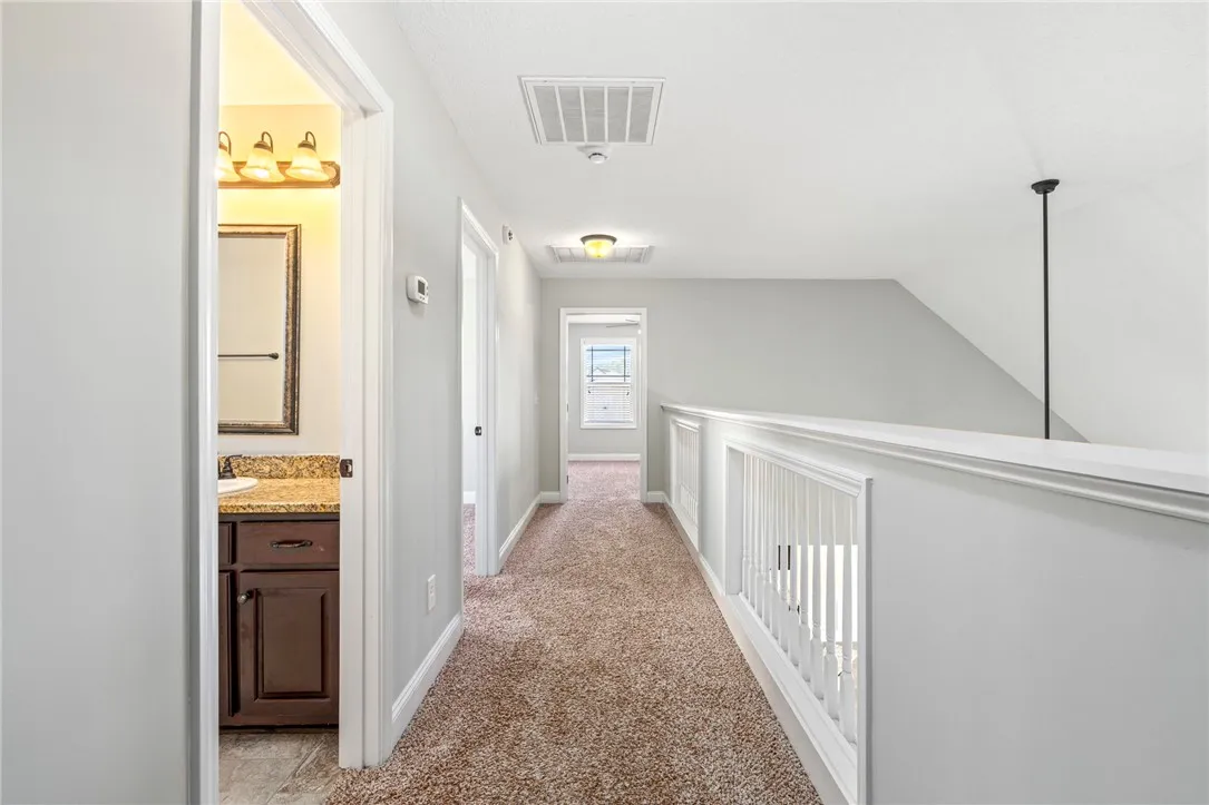 A spacious upper-level landing features soft carpeting and a partial view of an adjacent bathroom.