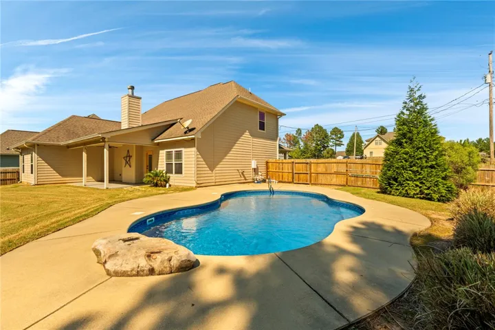 A spacious backyard patio surrounds a sparkling swimming pool under clear blue skies.