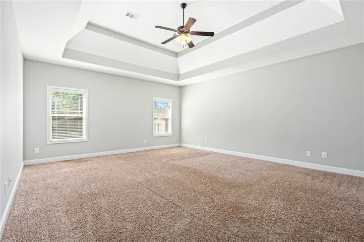 An elegant tray ceiling anchors this neutral bedroom with classic plush carpeting.