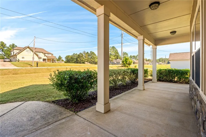 A spacious covered concrete porch overlooks the grassy front lawn and neighboring landscape.