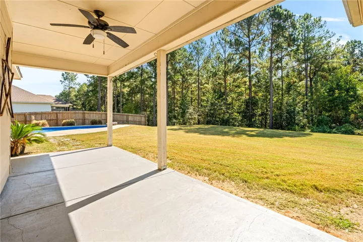 An inviting covered concrete patio overlooks a grassy backyard framed by mature trees.