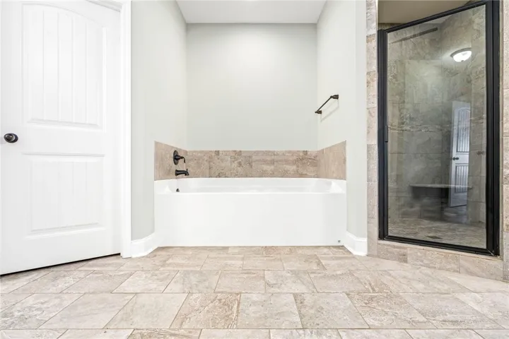 Fine tile flooring flows past a deep soaking tub toward a glass-enclosed walk-in shower.