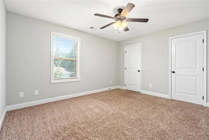 A window overlooks the outdoors in this bedroom featuring plush carpeting.