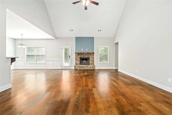 Rich hardwood flooring complements a striking floor-to-ceiling stone fireplace under towering vaulted ceilings.