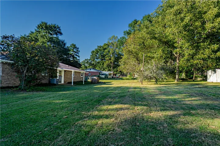 Mature trees frame a sprawling, level lawn behind the brick residence.