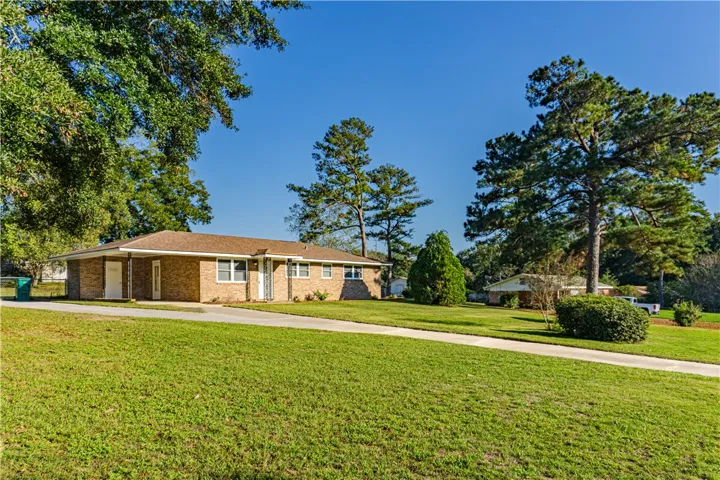 An expansive green lawn surrounds this classic brick ranch home framed by mature shade trees.