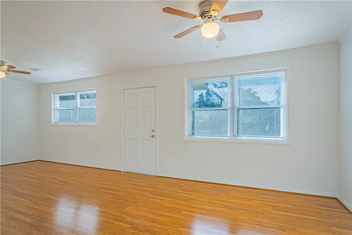 Polished hardwood floors anchor this light-filled room featuring multiple windows and an exterior door.