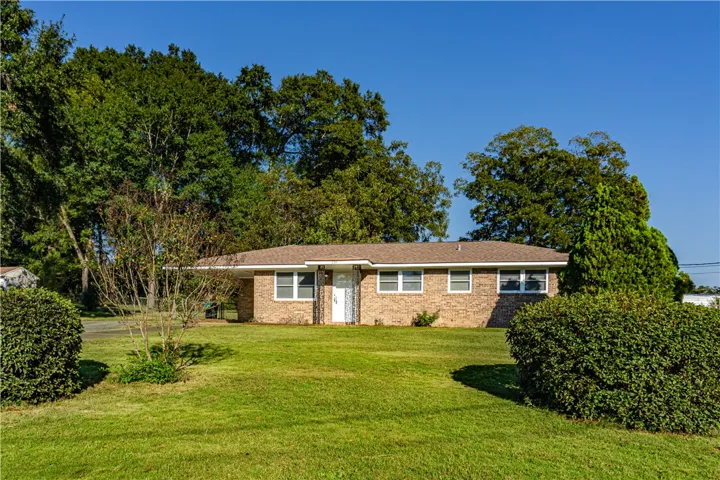 An inviting classic brick ranch exterior framed by mature trees and a manicured green lawn.