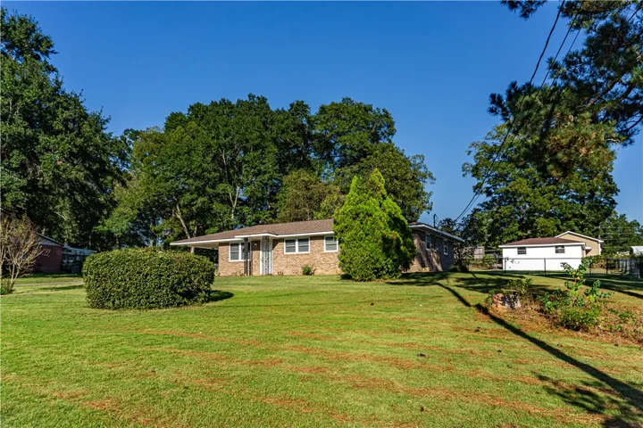 An expansive green lawn sweeps toward a classic brick ranch-style home framed by mature trees.