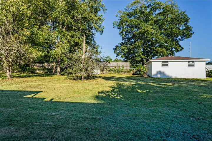 Mature trees shade a level grassy lawn bordering a detached white outbuilding.