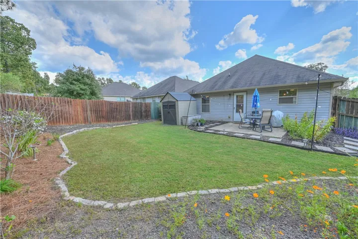 An inviting backyard features a level lawn, stone-bordered garden beds, and a paved patio area.