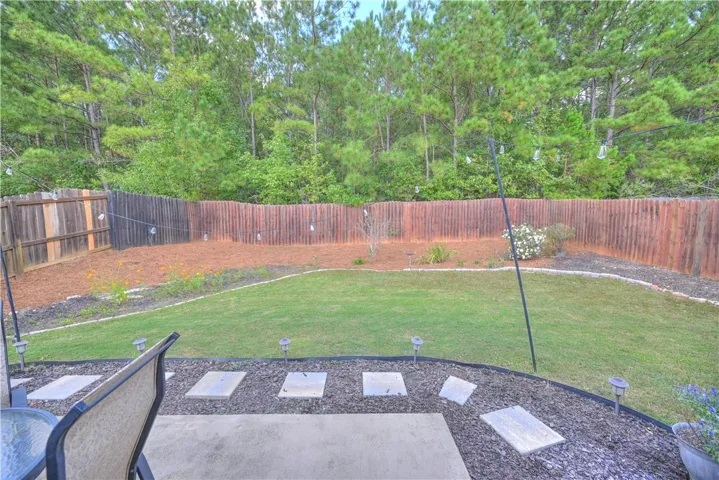 A spacious lawn area meets a natural tree line beyond the sturdy perimeter fencing.