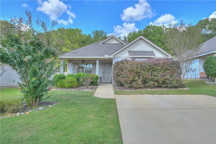A concrete driveway leads to this charming single-story home nestled against a mature tree line.