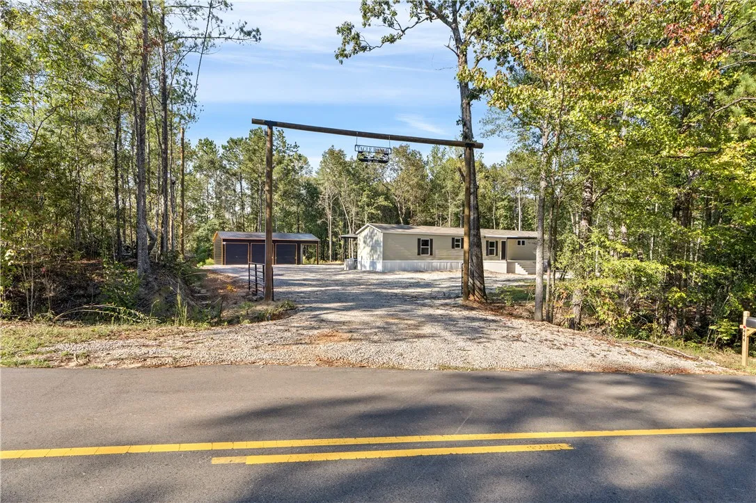 A private gravel driveway framed by mature trees leads to the main residence and detached garage.