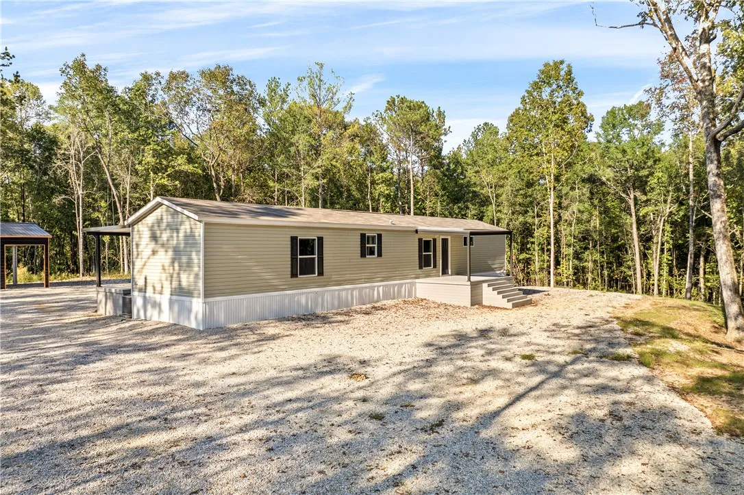 Mature trees frame a quiet clearing surrounding this modular home with vinyl siding.