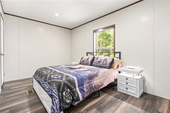 A quiet bedroom features wood-style flooring and a window framing leafy outdoor views.