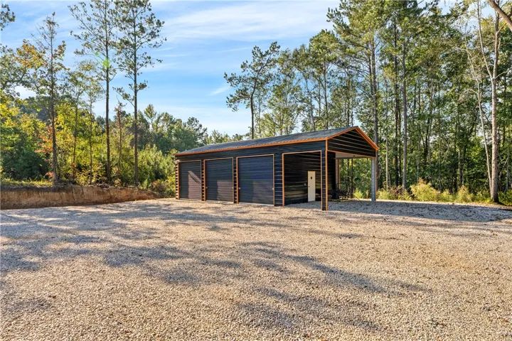 A spacious multi-bay workshop sits nestled against a lush backdrop of mature pine trees.