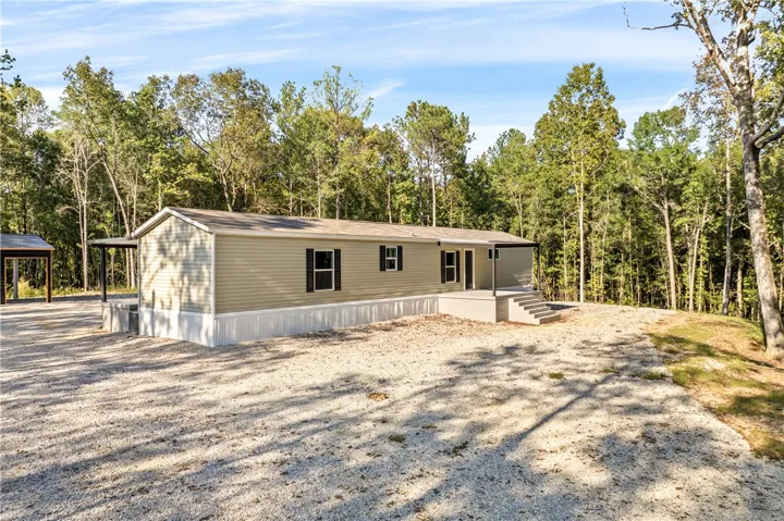 Mature trees frame a quiet clearing surrounding this modular home with vinyl siding.