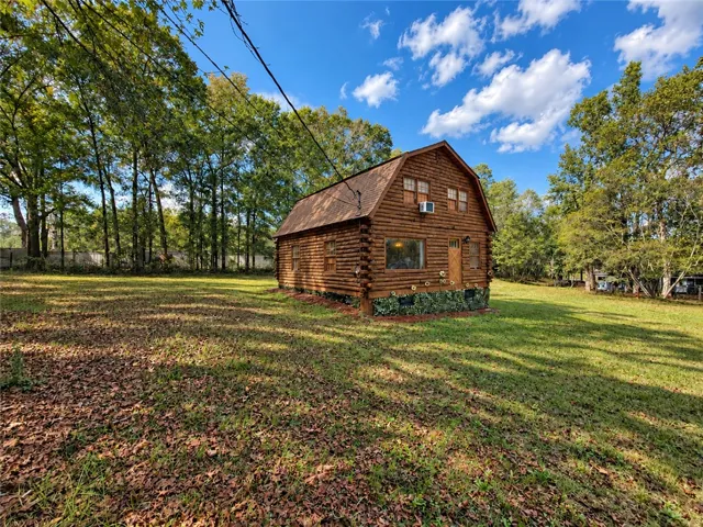 A rustic log home sits nestled on a grassy clearing bordered by mature trees.