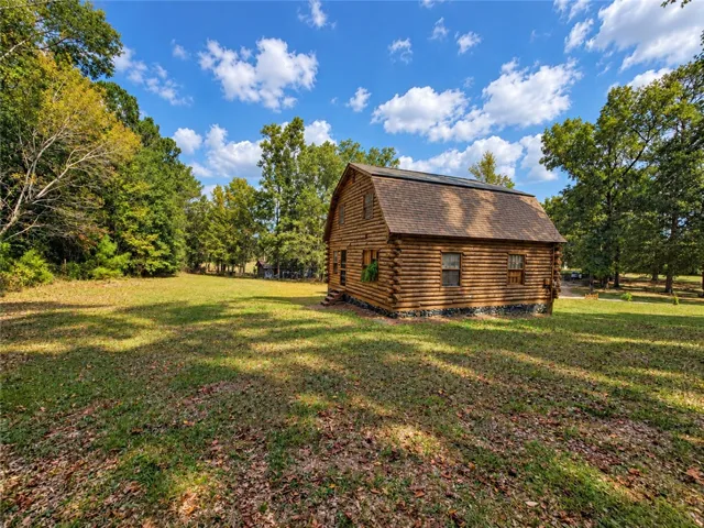 Rustic log architecture stands amidst mature trees on a sprawling grassy clearing.