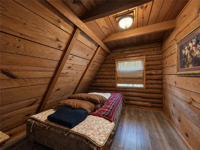 Rich wood planking and log walls define this cozy bedroom under a vaulted ceiling.