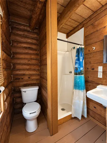 Rustic charm defines this bathroom featuring exposed log walls and a beamed wood ceiling.