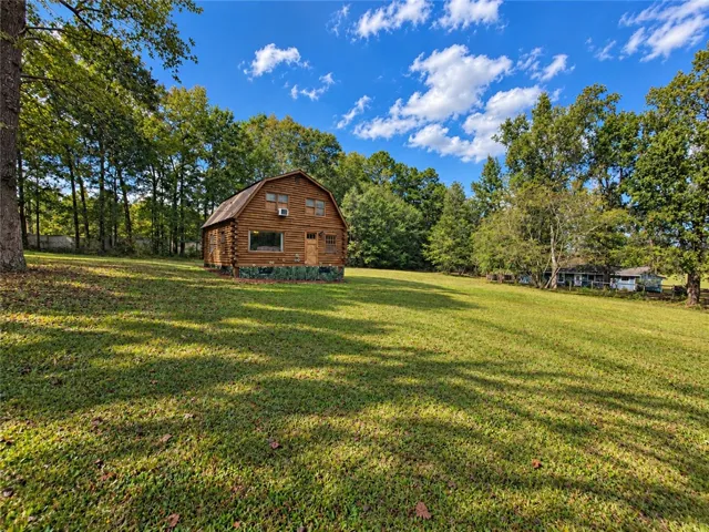 A rustic log home stands nestled among towering trees on a vast grassy clearing.
