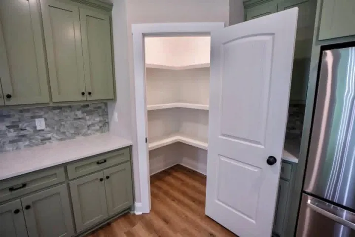 A walk-in pantry with wrap-around shelving sits adjacent to custom cabinetry and stone counters.