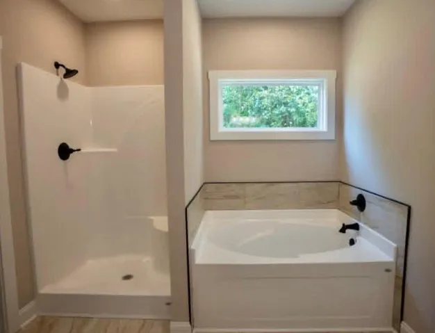 A built-in soaking tub and adjacent walk-in shower stand beneath a high window.