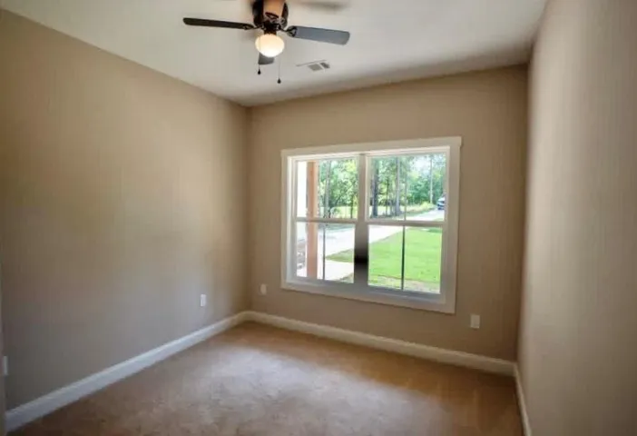 A spacious secondary bedroom features soft carpeting, high ceilings, and views of the verdant yard.