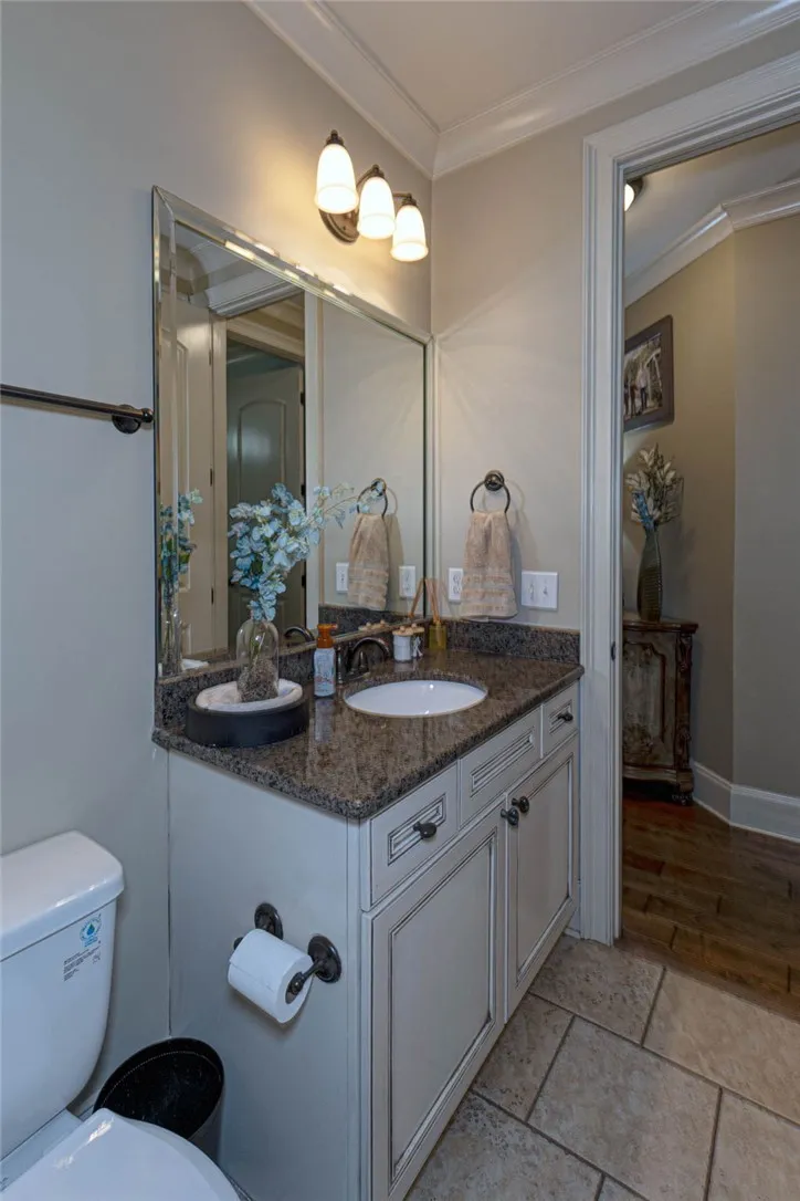 A refined powder room features a granite-topped vanity, classic crown molding, and timeless tile flooring.