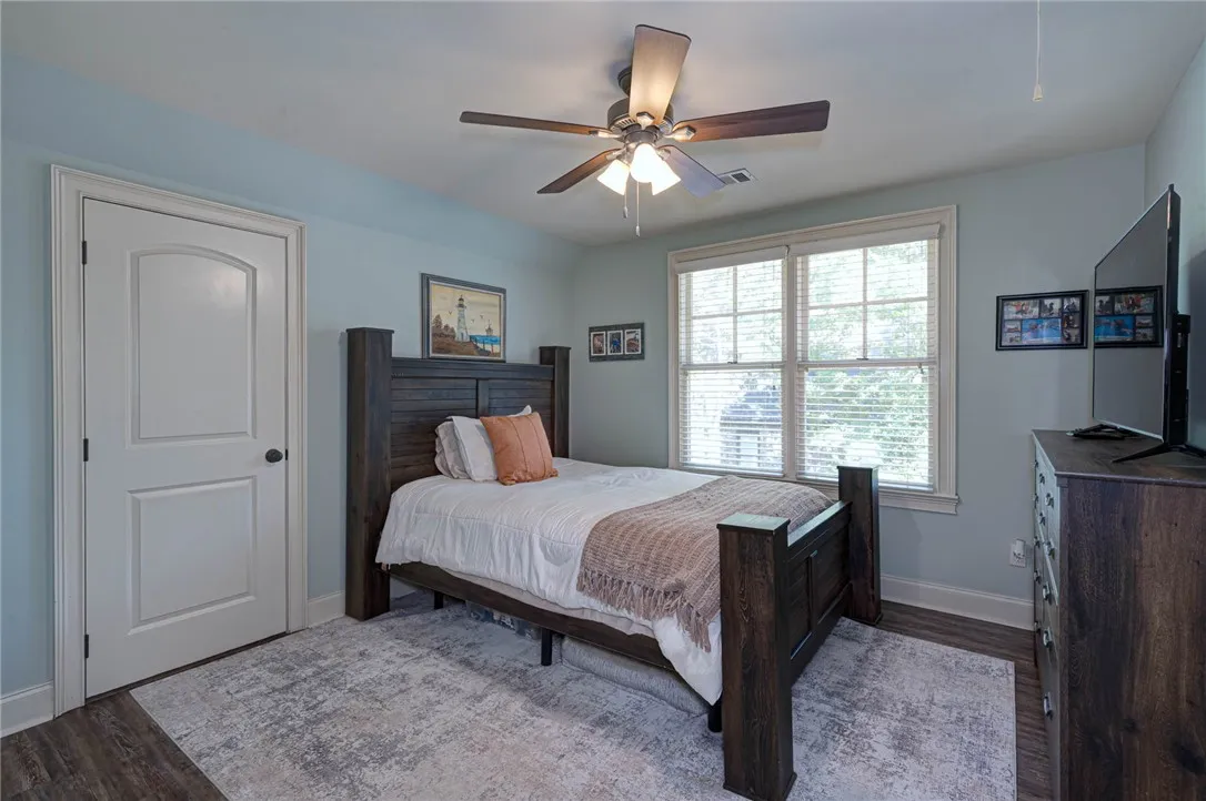 Double-hung windows frame neighborhood views in this light-filled bedroom featuring durable wood flooring.