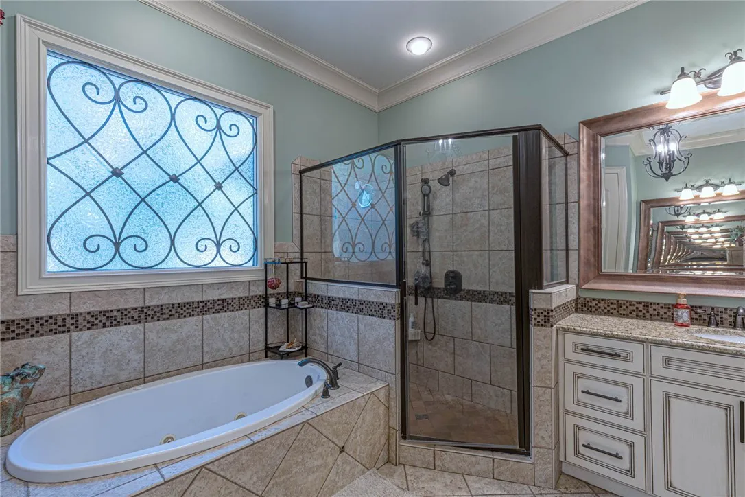 An elegant soaking tub and walk-in shower are framed by detailed tilework and crown molding.
