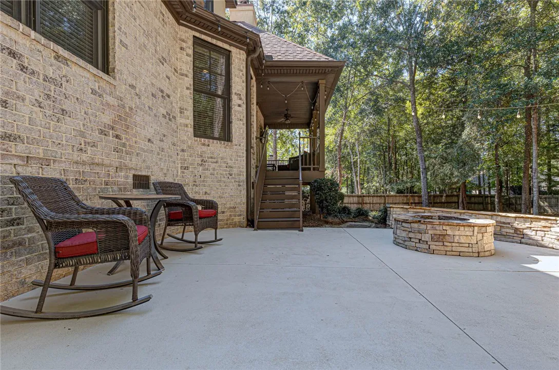 An expansive concrete patio features a built-in stone fire pit set against a brick exterior.